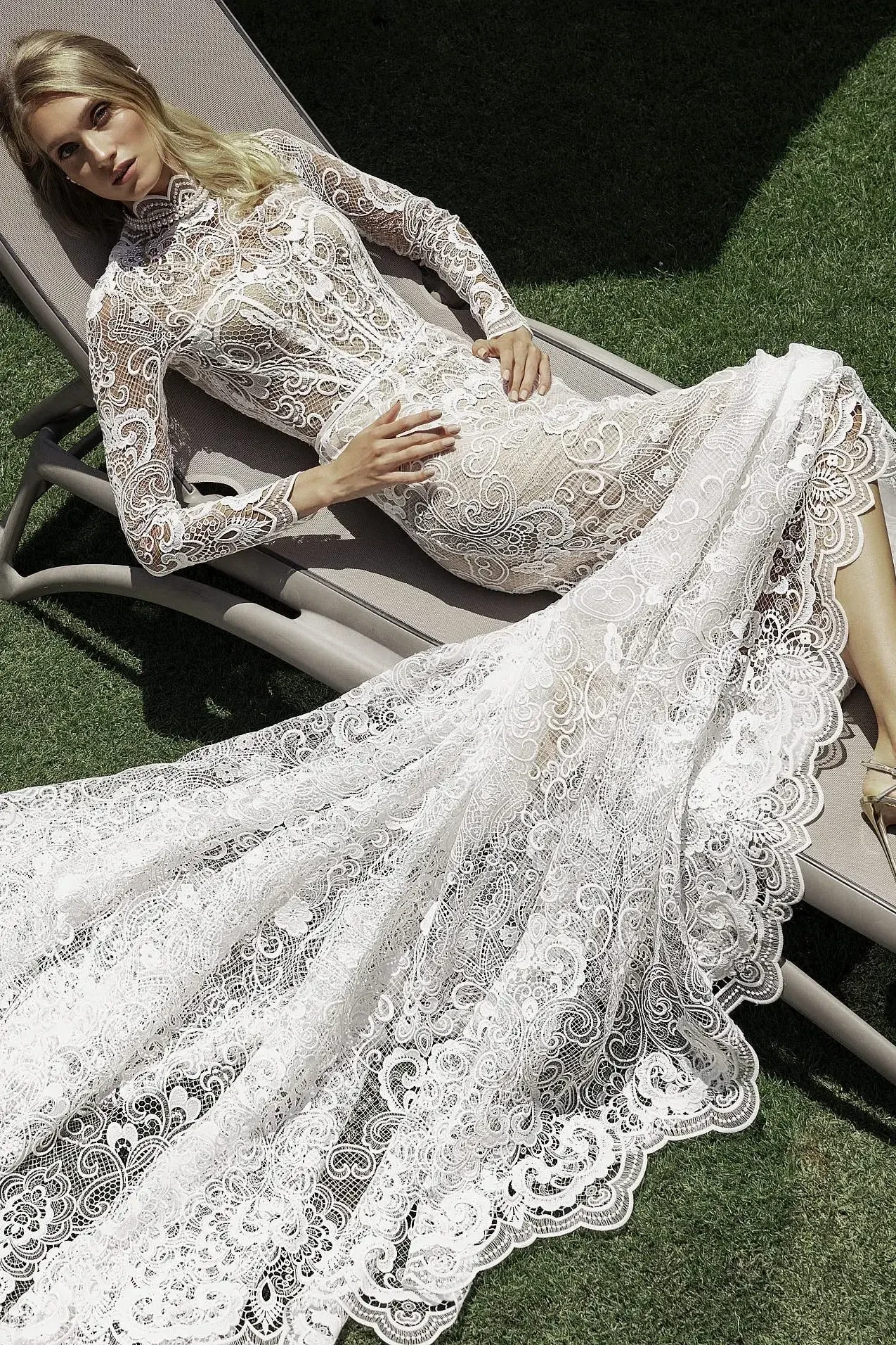 Model is wearing a long-sleeve fitted gown with a high scalloped neckline, sheer corset, crochet lace, pearl embellishments, and a scalloped-edge train.