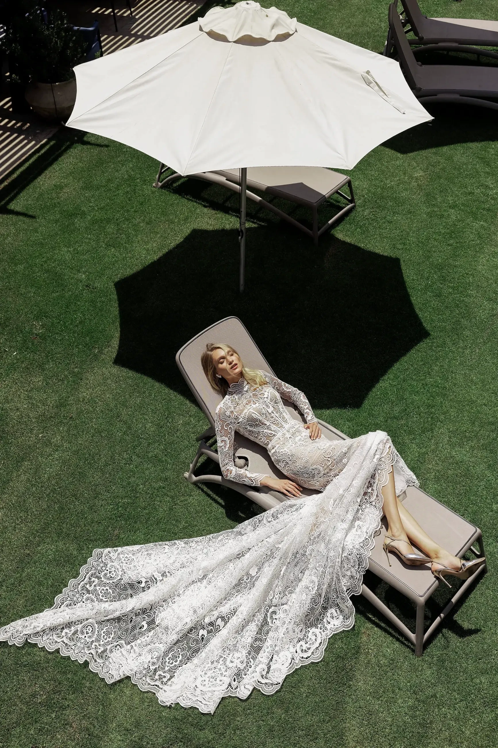 Model is wearing a long-sleeve fitted gown with a high scalloped neckline, sheer corset, crochet lace, pearl embellishments, and a scalloped-edge train.