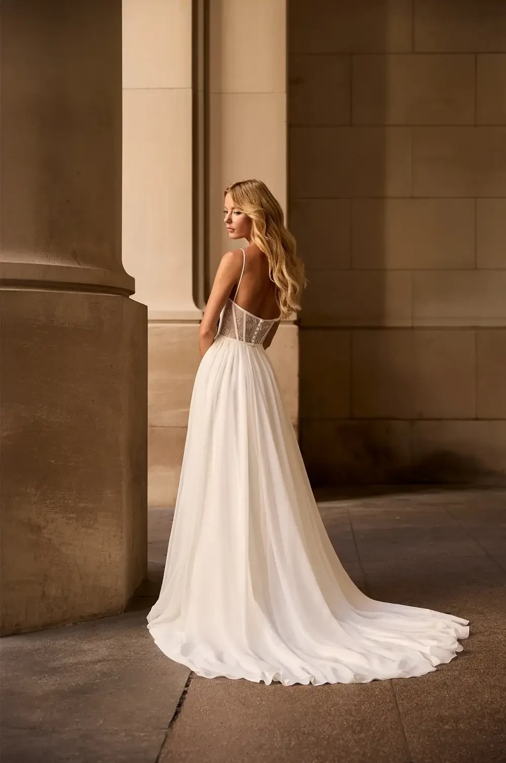 A woman in a flowing white dress standing near a stone column, looking back over her shoulder.