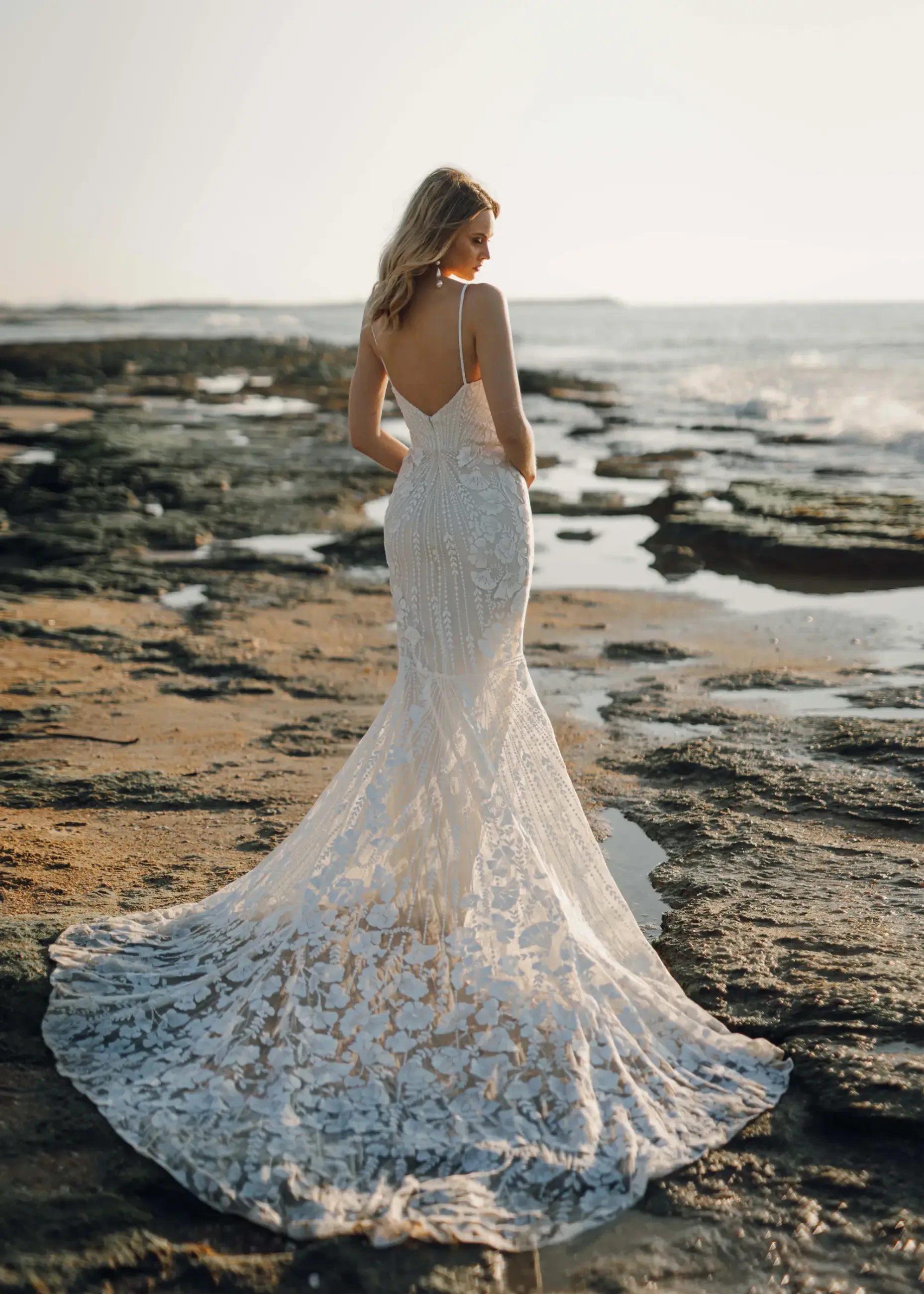 Model is wearing a bohemian wedding dress with spaghetti straps, a notched neckline, and sequin botanical lace by rish