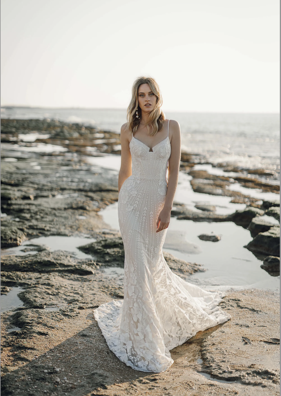Model is wearing a bohemian wedding dress with spaghetti straps, a notched neckline, and sequin botanical lace by rish